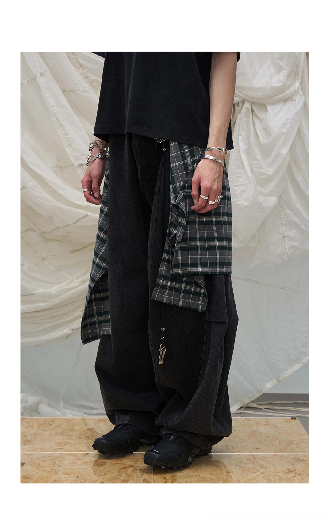 Side view of dark balloon leg denim pants with a plaid layer tied at the waist and oversized black t-shirt