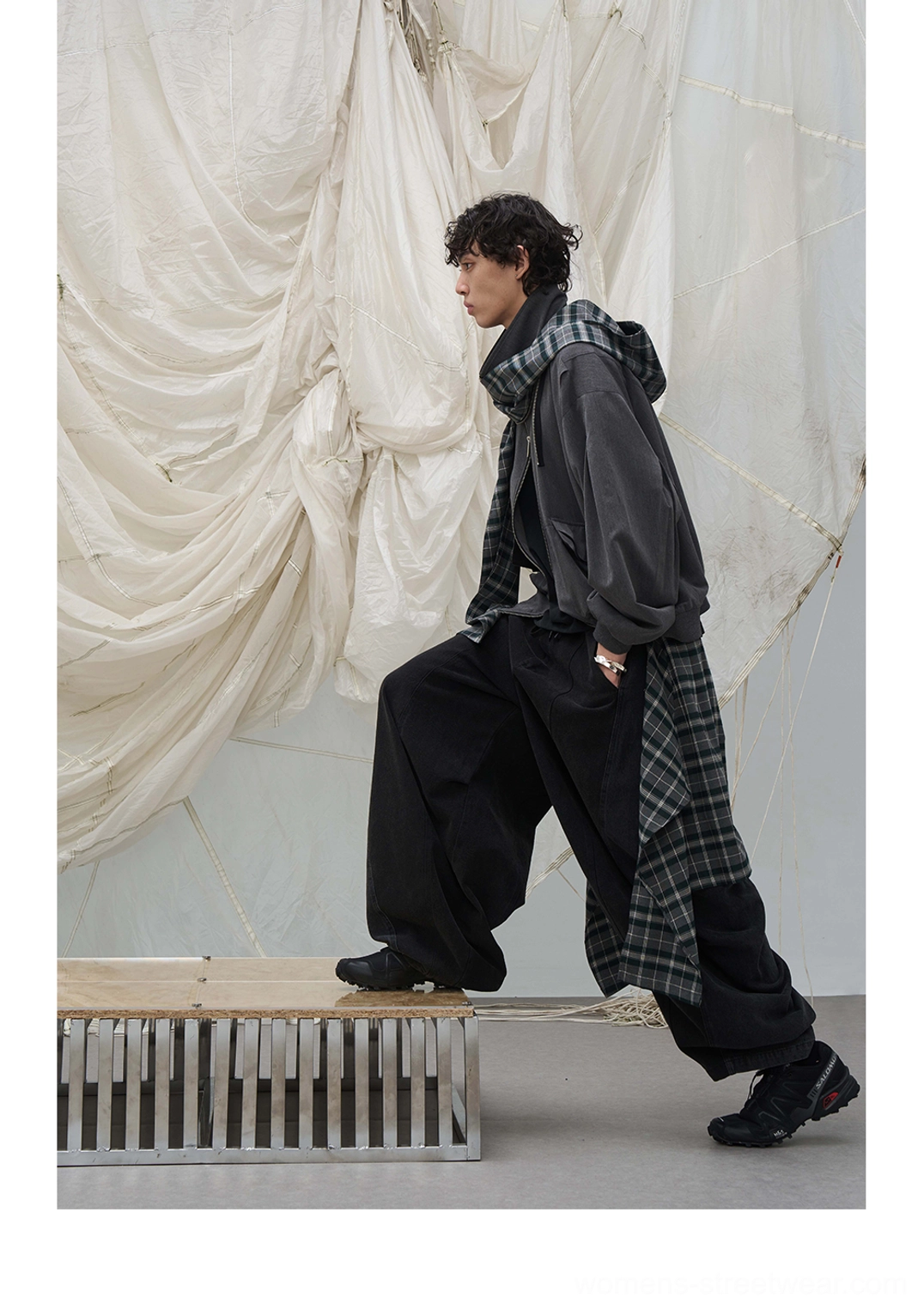 Side stepping view of washed black balloon leg denim pants with draped plaid waist layer in a streetwear studio outfit