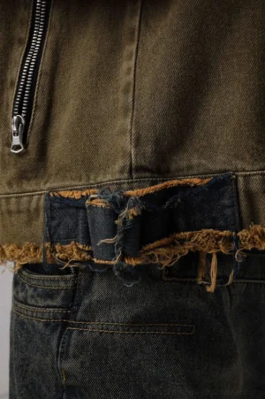 Close-up detail of distressed applique denim jacket showing metal zipper hardware, frayed contrast denim patch, and utility pocket stitching