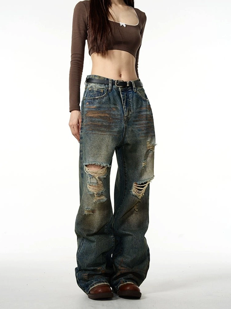 Female model wearing vintage blue distressed baggy ripped jeans with wide legs and knee rips in a front full-body streetwear outfit