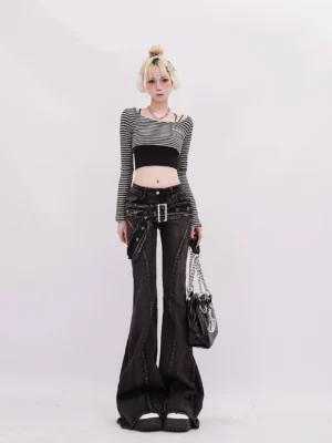 Female model wearing distressed black gray wash flared jeans with a detachable belt and raw hems styled with a striped crop top for Y2K streetwear