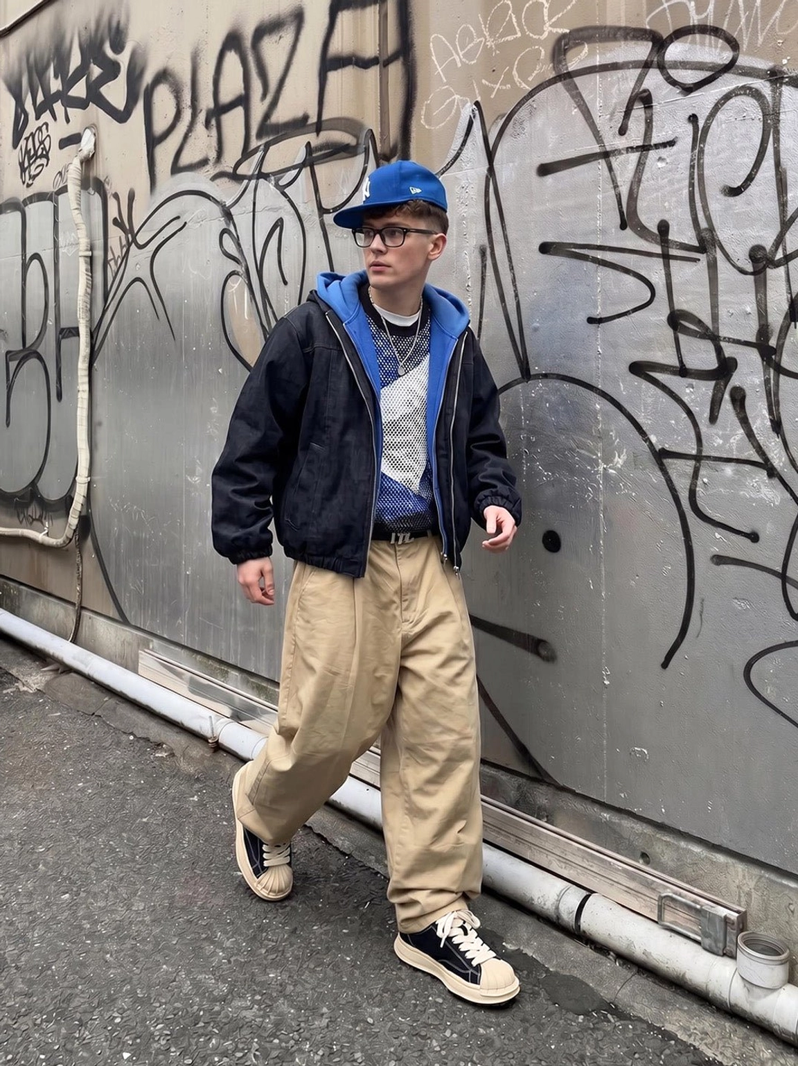Distressed black shell-toe platform sneakers styled with a navy jacket and khaki pants against a graffiti street wall