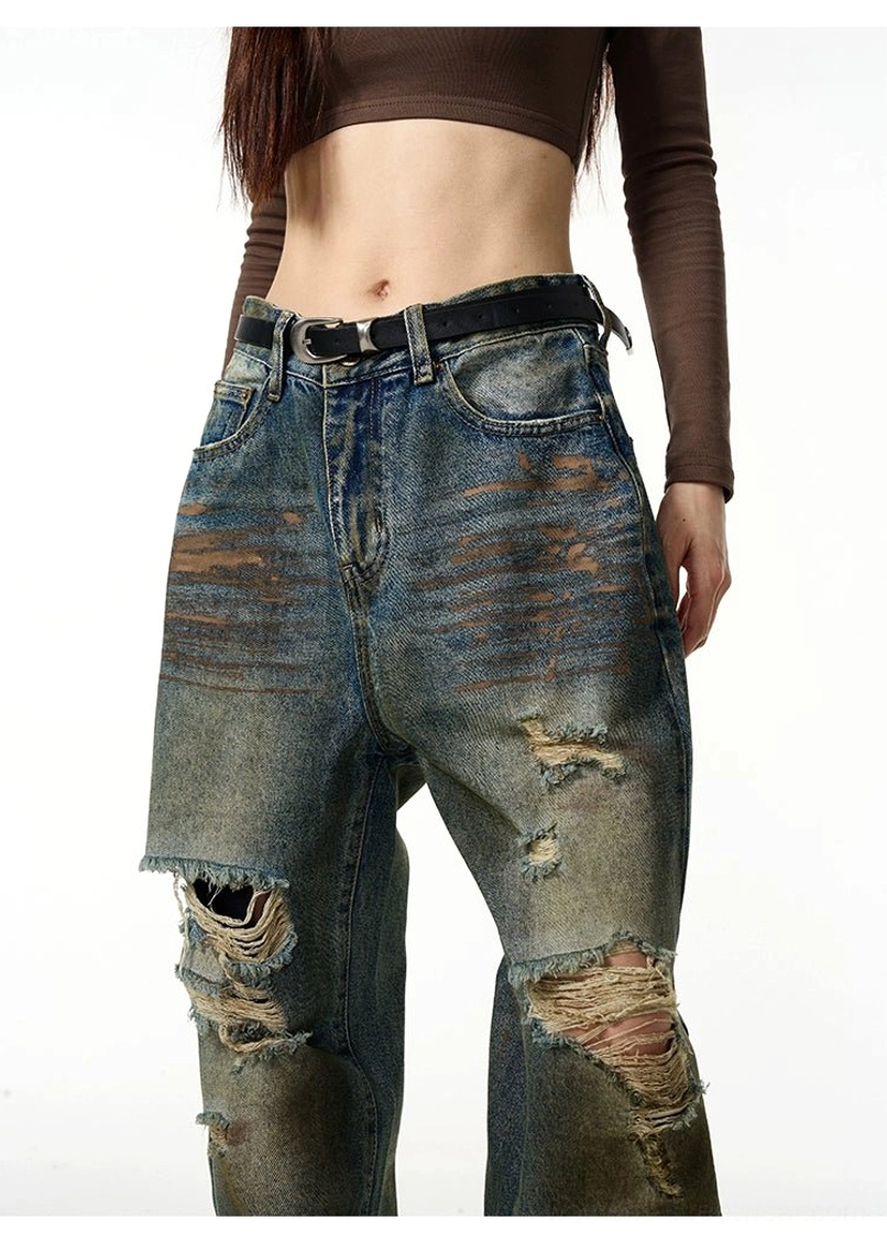 Close-up front view of distressed blue denim jeans showing belt loops, button zip closure, pockets, and ripped knee details