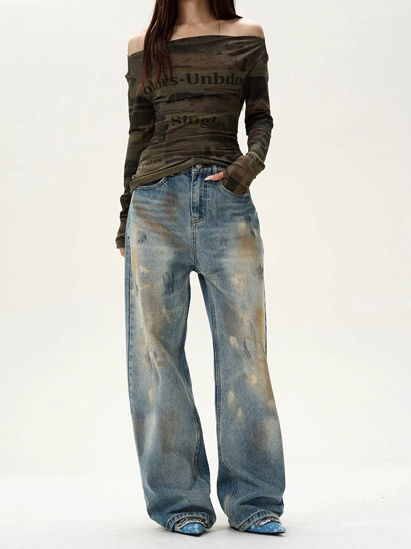 Female model wearing distressed blue wide-leg baggy jeans with vintage washed denim, brown distressed details, and a relaxed Y2K streetwear silhouette