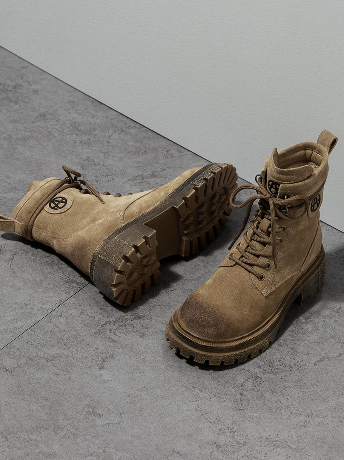 Brown distressed combat boots oblique angle display gray concrete texture background one boot flat showing outsole other front view heel pull tab