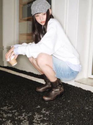 Model wearing distressed brown harness western mid-calf boots with denim shorts in an outdoor streetwear look
