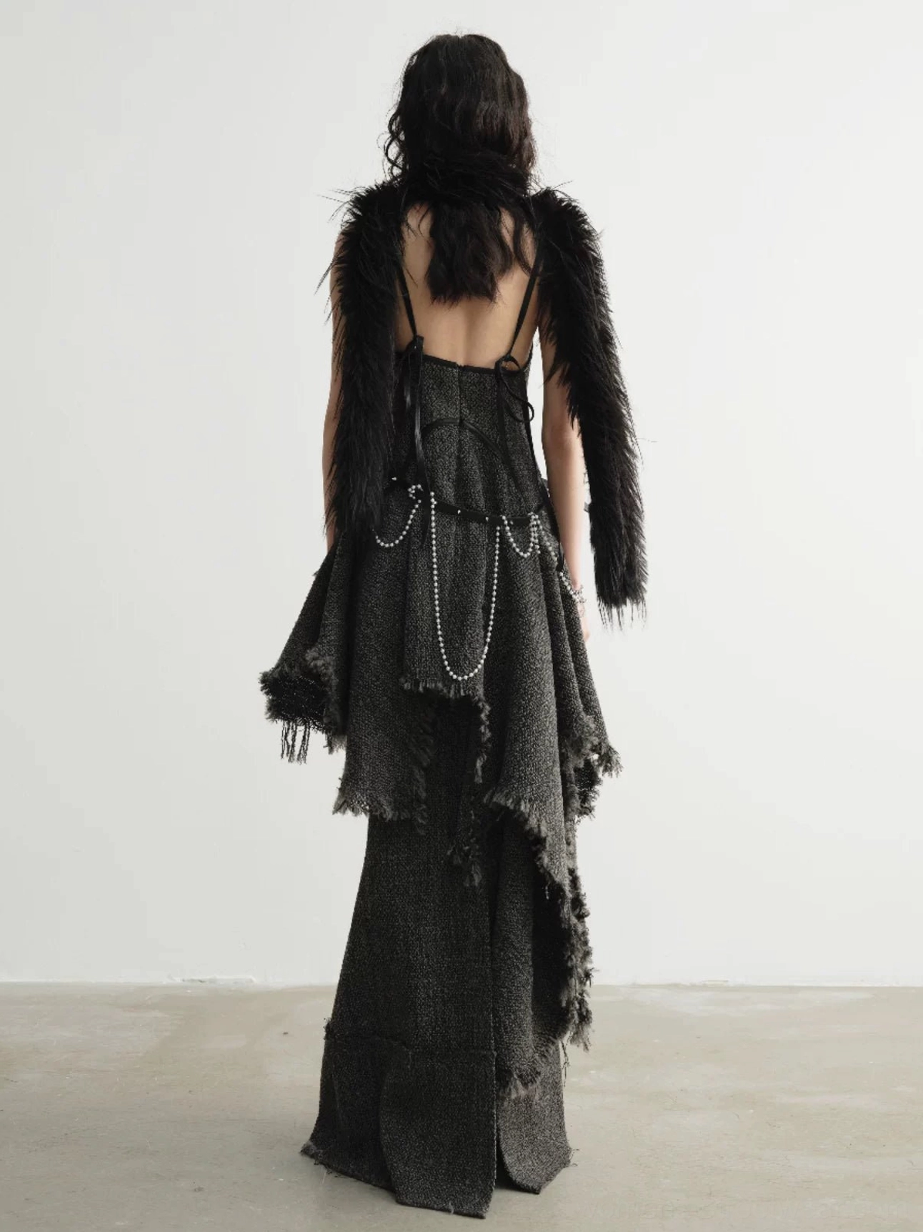 Back view of distressed charcoal tweed mermaid maxi skirt styled with layered accessories in a minimalist studio