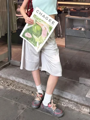 Female model wearing distressed contrast stitch PU low-top streetwear shoes with wide-leg shorts on outdoor storefront steps