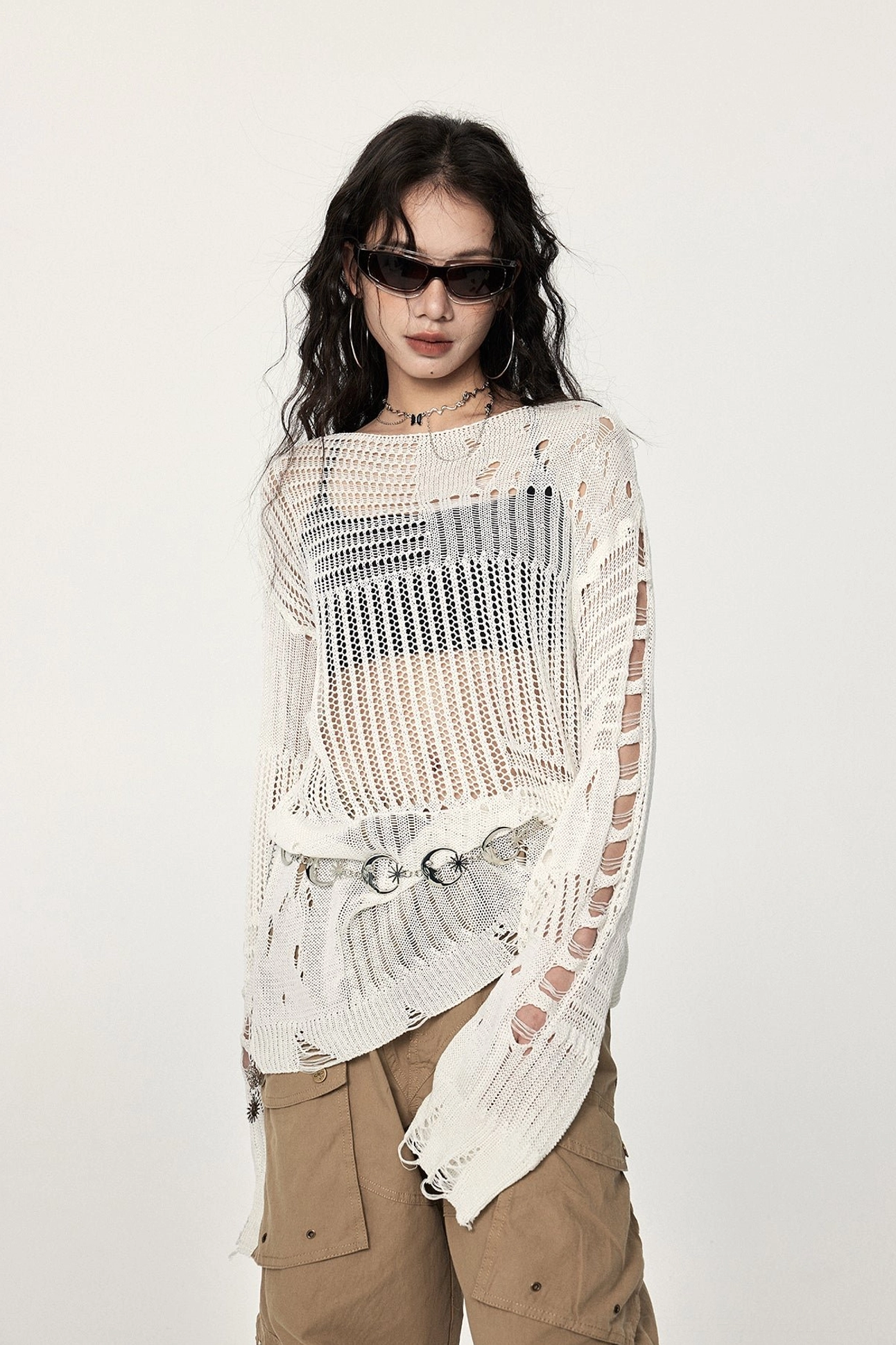 Three-quarter view of a loose off-white crochet streetwear sweater with distressed sleeve slits, open knit panels, and industrial metal waist accents