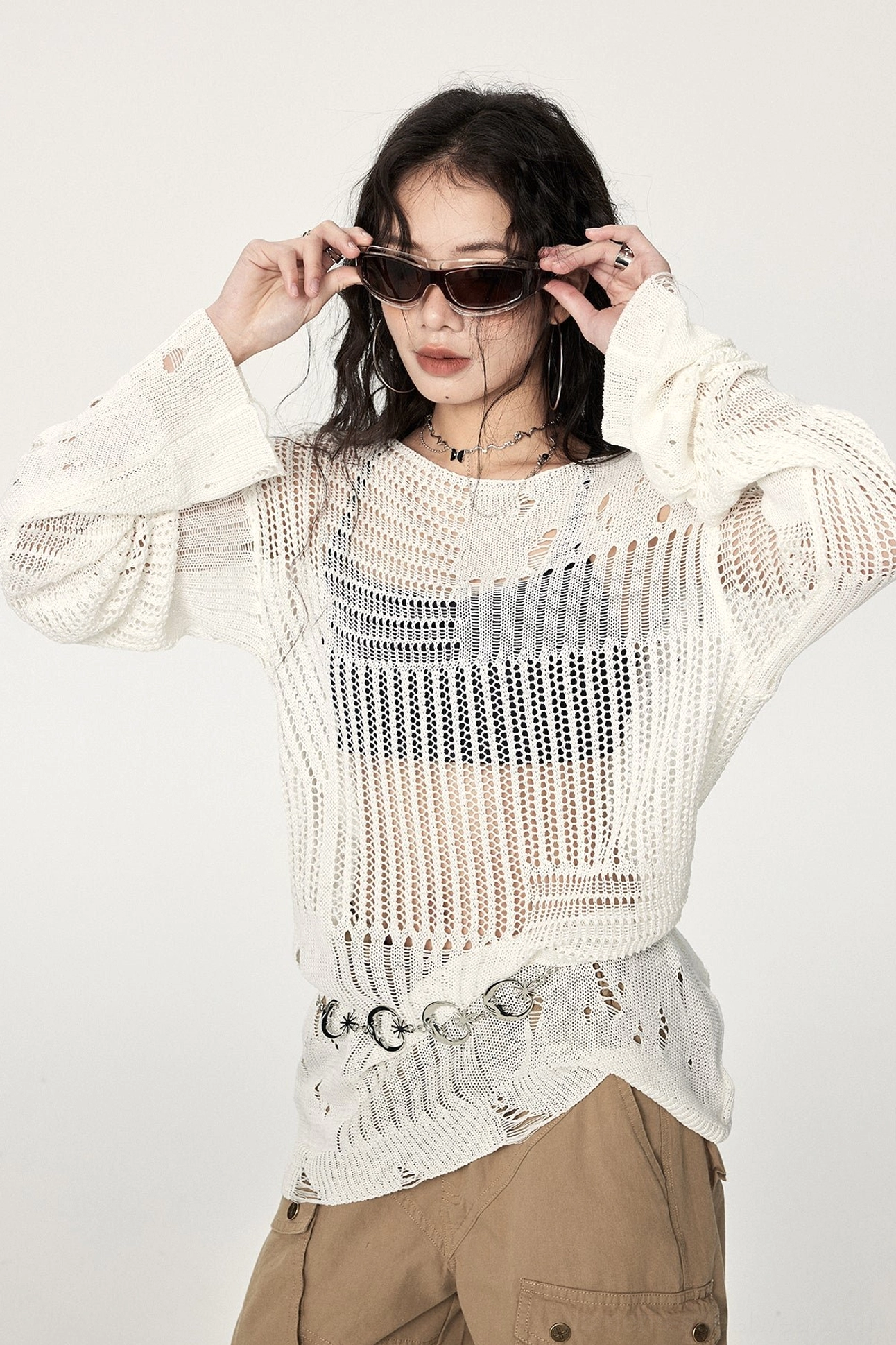 Close-up of a wide crew neck distressed crochet sweater showing exposed layering, uneven hem, open knit texture, and ripped sleeve details