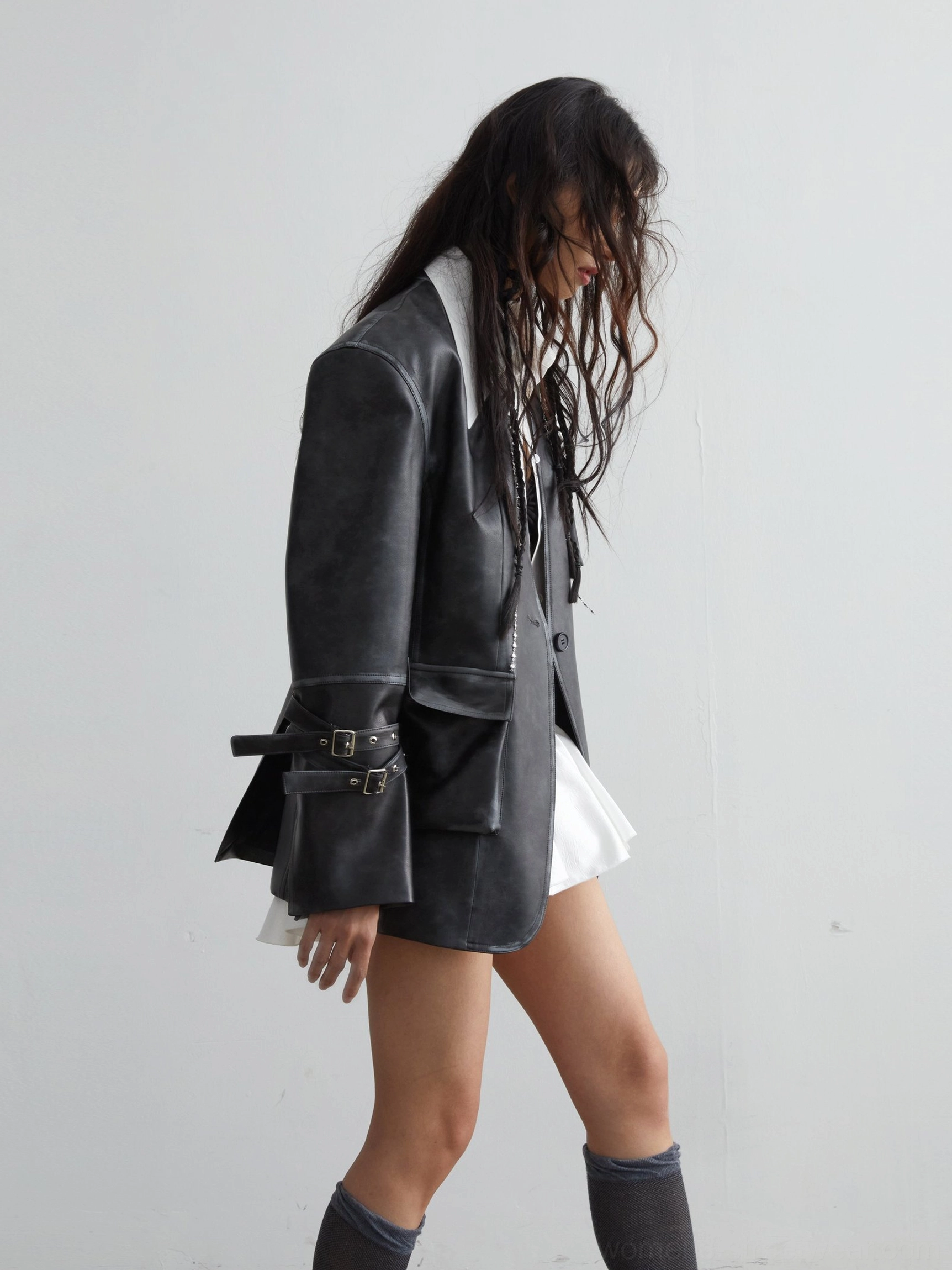 Right side profile of a distressed dark-grey PU leather utility jacket with chest pockets, oversized shoulders, and adjustable cuffs