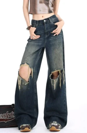 Front full-body view of distressed dark wash wide leg ripped jeans with a high waist, oversized frayed knee openings, vintage gradient denim wash, cropped top, leather shoes, and retro streetwear styling