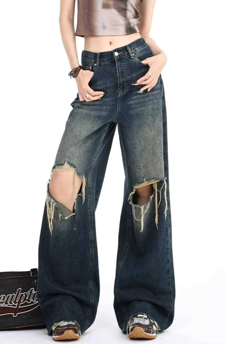 Front full-body view of distressed dark wash wide leg ripped jeans with a high waist, oversized frayed knee openings, vintage gradient denim wash, cropped top, leather shoes, and retro streetwear styling