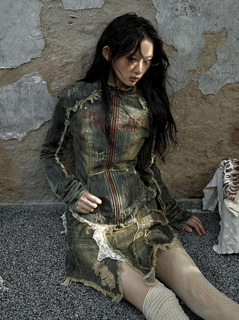 Seated streetwear styling featuring a frayed distressed denim corset jacket, lace-trim skirt, and sheer tights