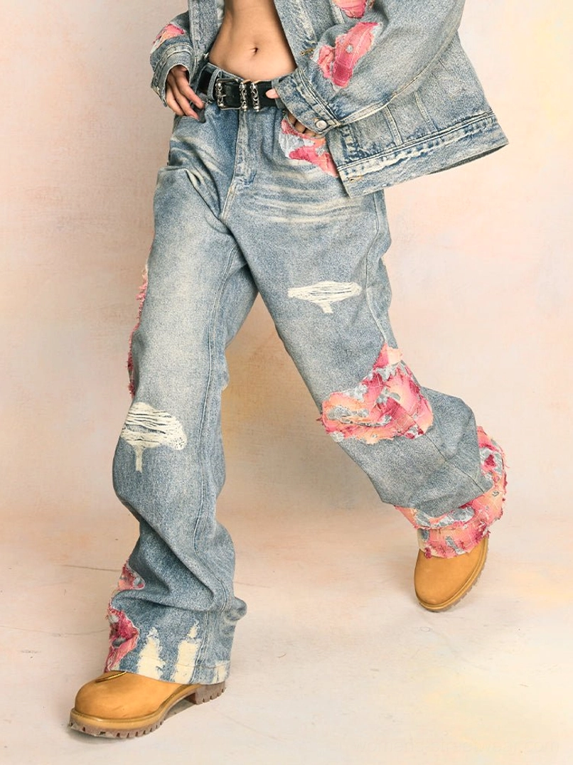 Female model wearing a coordinated distressed denim jacket and pink-accented wide-leg jeans outfit with tan boots