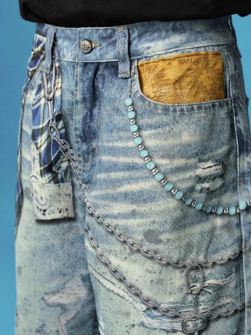 Close-up of distressed blue denim jorts showing metal button, layered chains, turquoise bead trim, lace patch, pocket detail, and worn streetwear texture
