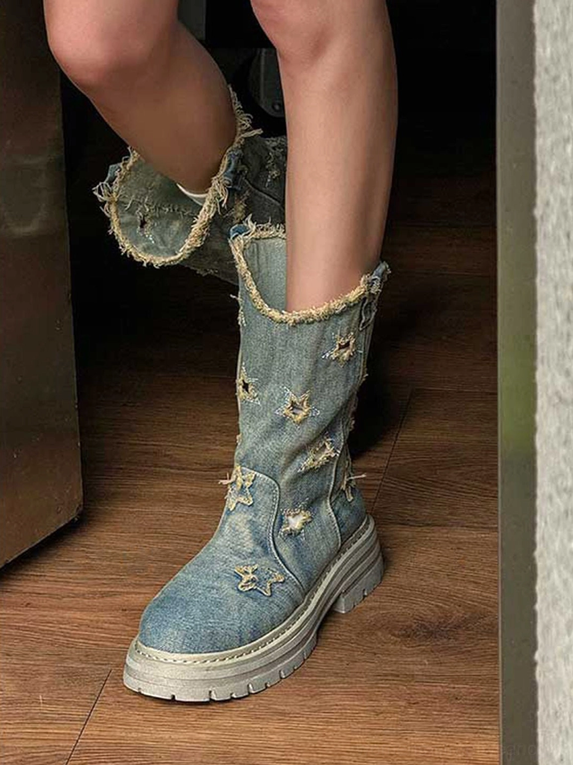Close-up of distressed denim mid-calf platform boots worn with star-shaped cutouts, frayed cuff, and chunky gray rubber sole