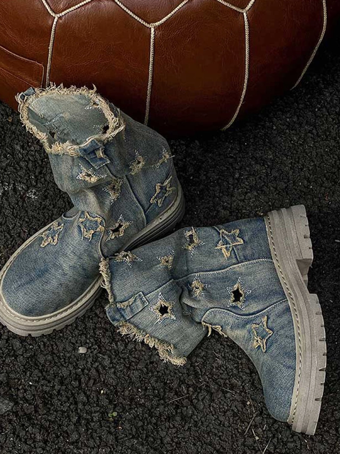 Overhead flat lay of two distressed denim platform boots with star embroidery, cutout details, frayed collars, and rugged tread