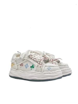 White distressed embroidered platform sneakers shown in a front side three quarter view with frayed canvas panels colorful clover and geometric embroidery twisted rope laces and thick dark edged streetwear sole