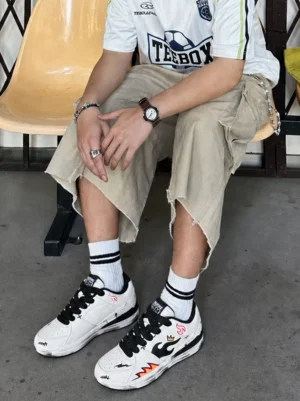 Male model styling white flame graphic distressed court sneakers with cropped cargo pants and striped socks