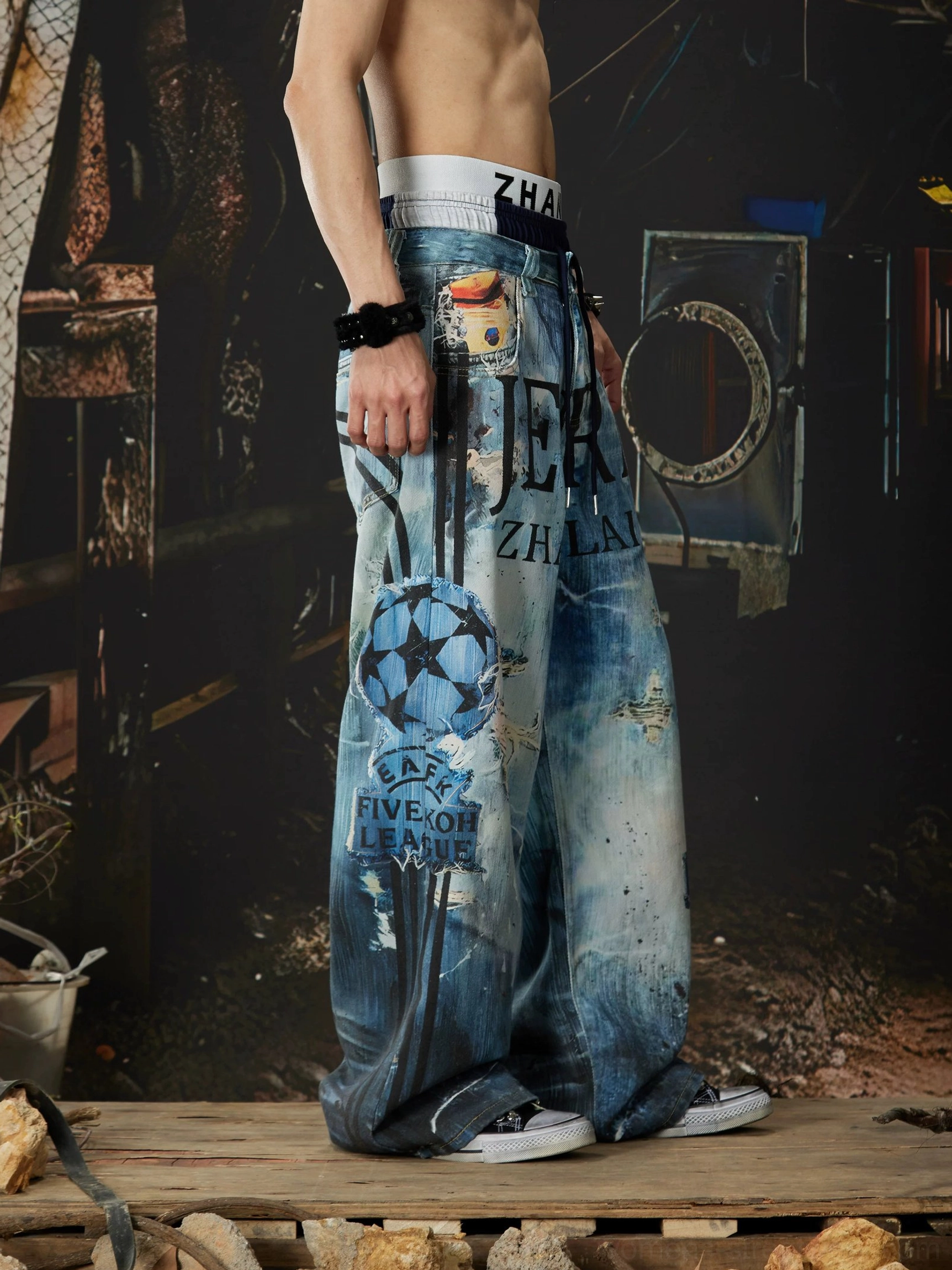 Left side view of distressed graffiti wide-leg jeans showing decorative side prints, faded ocean wash, roomy pockets, and vintage streetwear styling