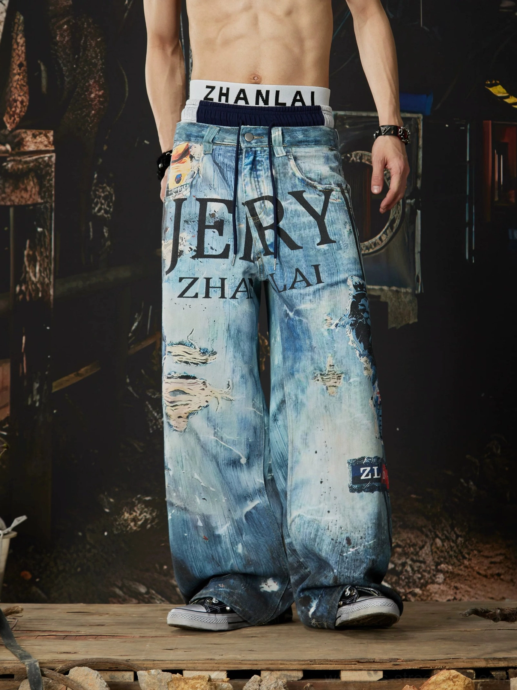 Right front view of blue distressed wide-leg jeans with side leg graphics, ribbed drawstring waistband, and relaxed urban streetwear cut
