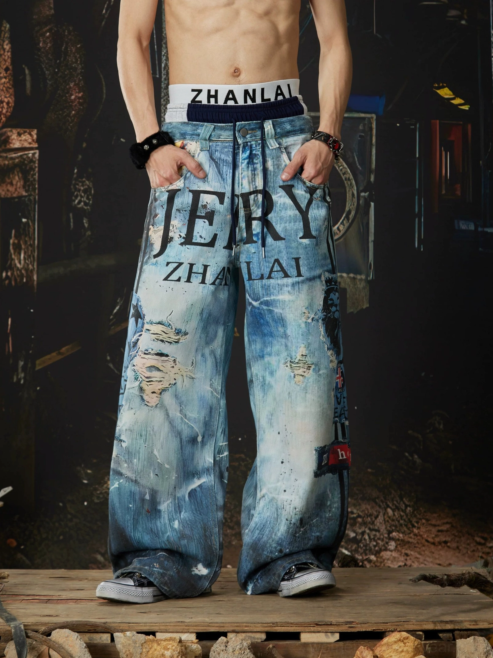 Front view of distressed ocean-blue wide-leg jeans with central letter graphics, multiple ripped details, and classic oversized denim fit