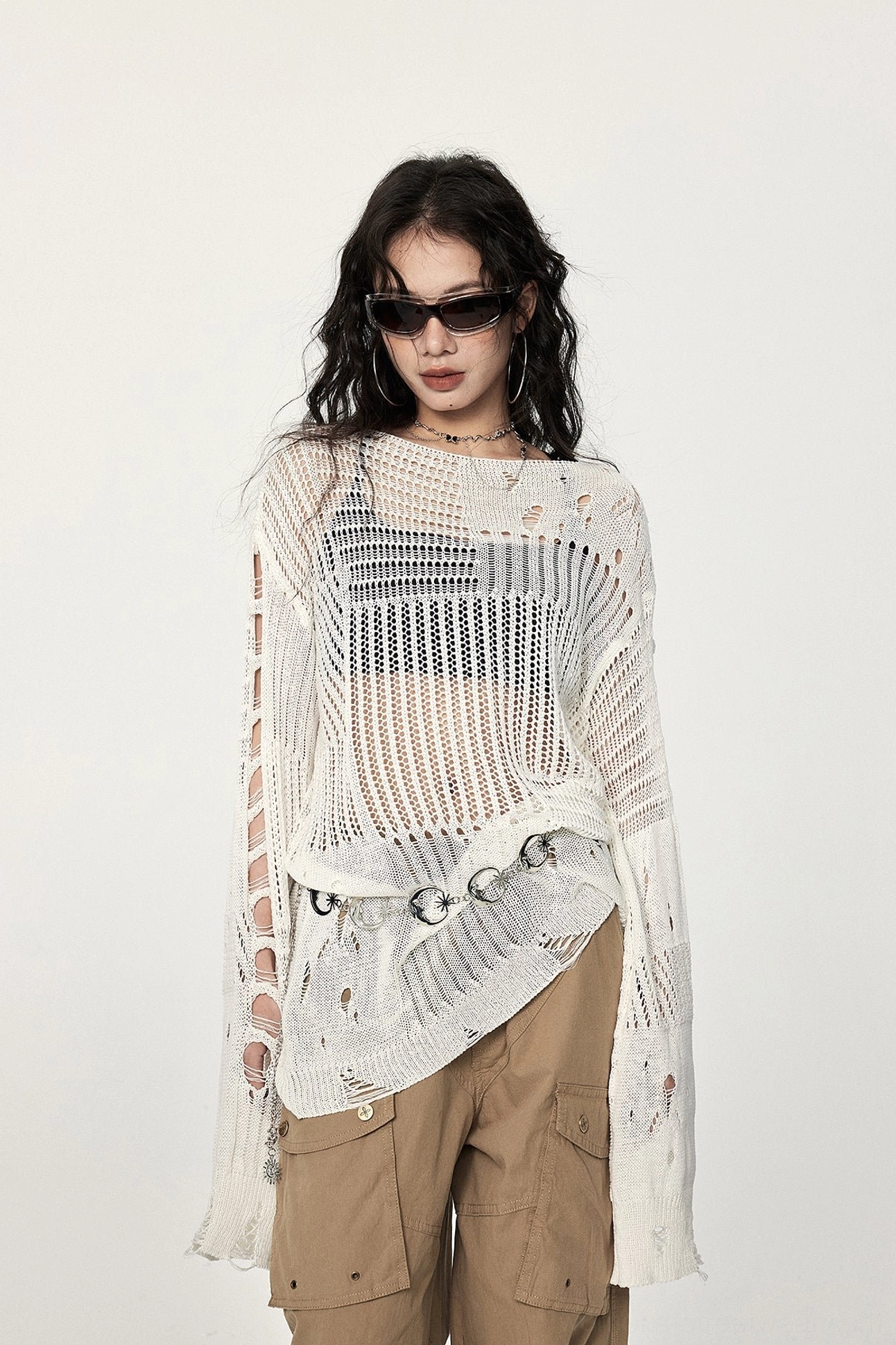 Front view of an off-white distressed hollow-out crochet sweater with asymmetric hem, ripped long sleeves, metal waist rings, and oversized streetwear fit
