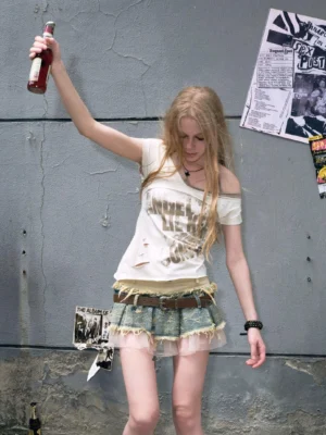 Front view of a distressed layered denim mini skirt with frayed patchwork edges, sheer tulle hem, brown belt, and graphic streetwear tee