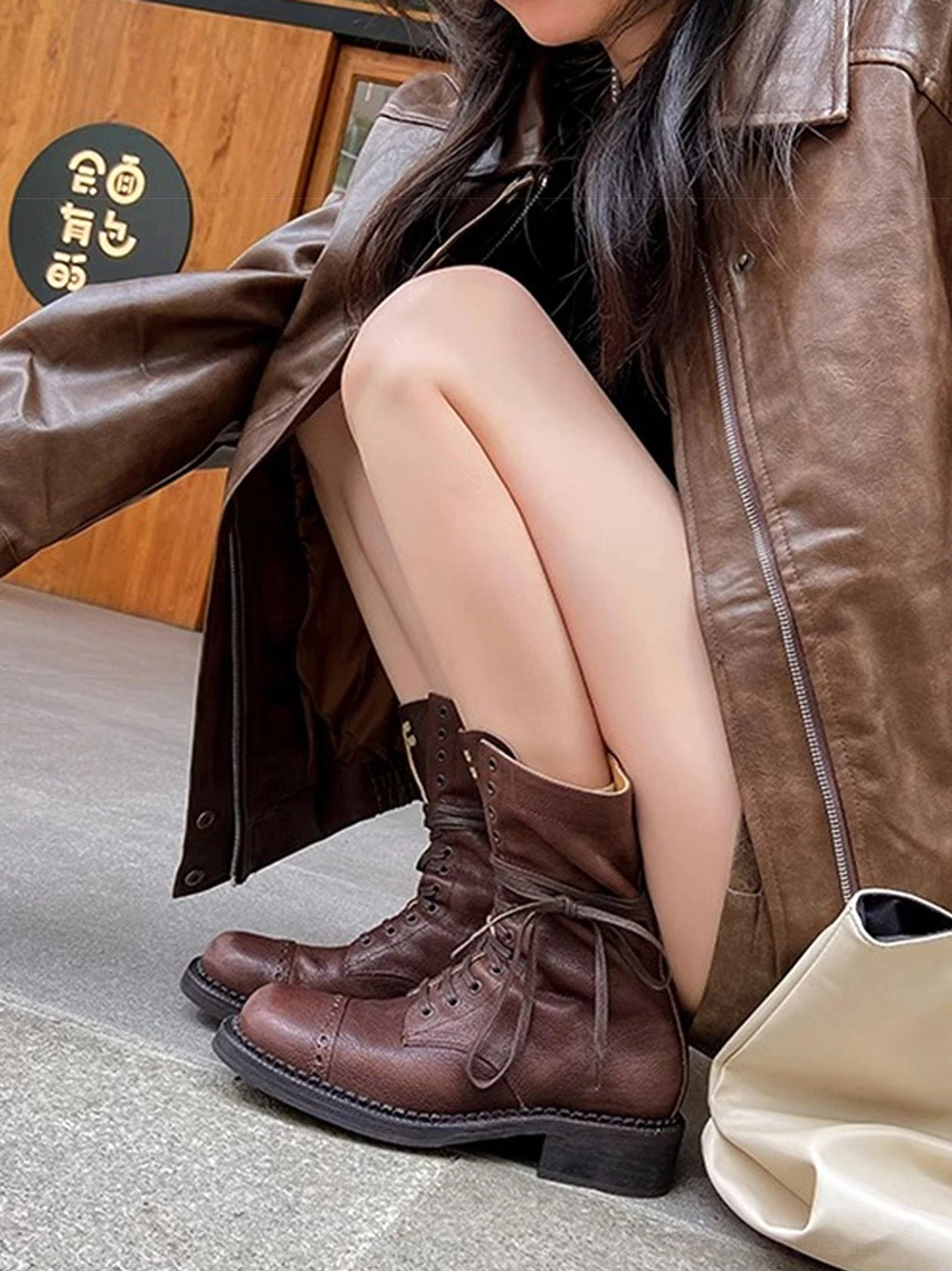 Dark brown mid-calf lace-up combat boots styled with leather handbag in indoor coffee shop streetwear outfit