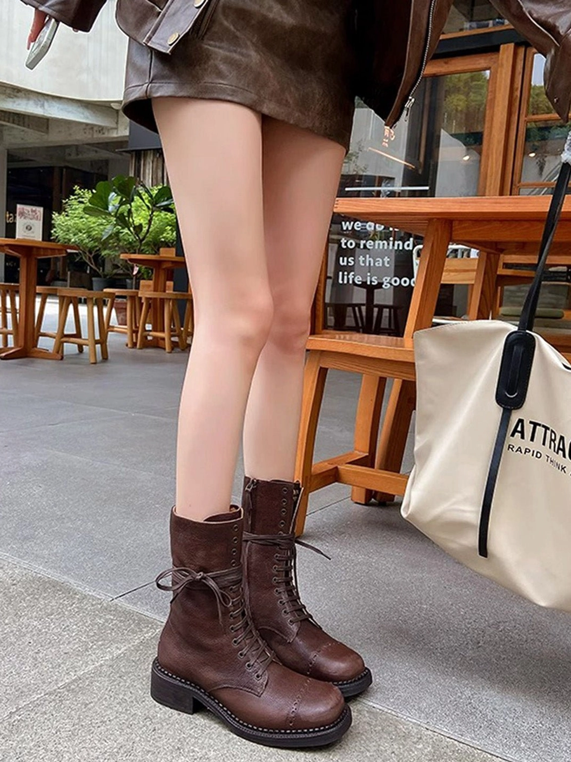 Dark brown lace-up mid-calf combat boots worn with matching brown two-piece outfit and canvas tote bag