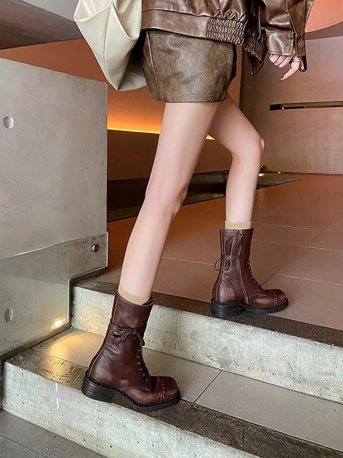 Dark brown distressed leather mid-calf combat boots worn with cropped leather jacket and mini skirt on stairwell