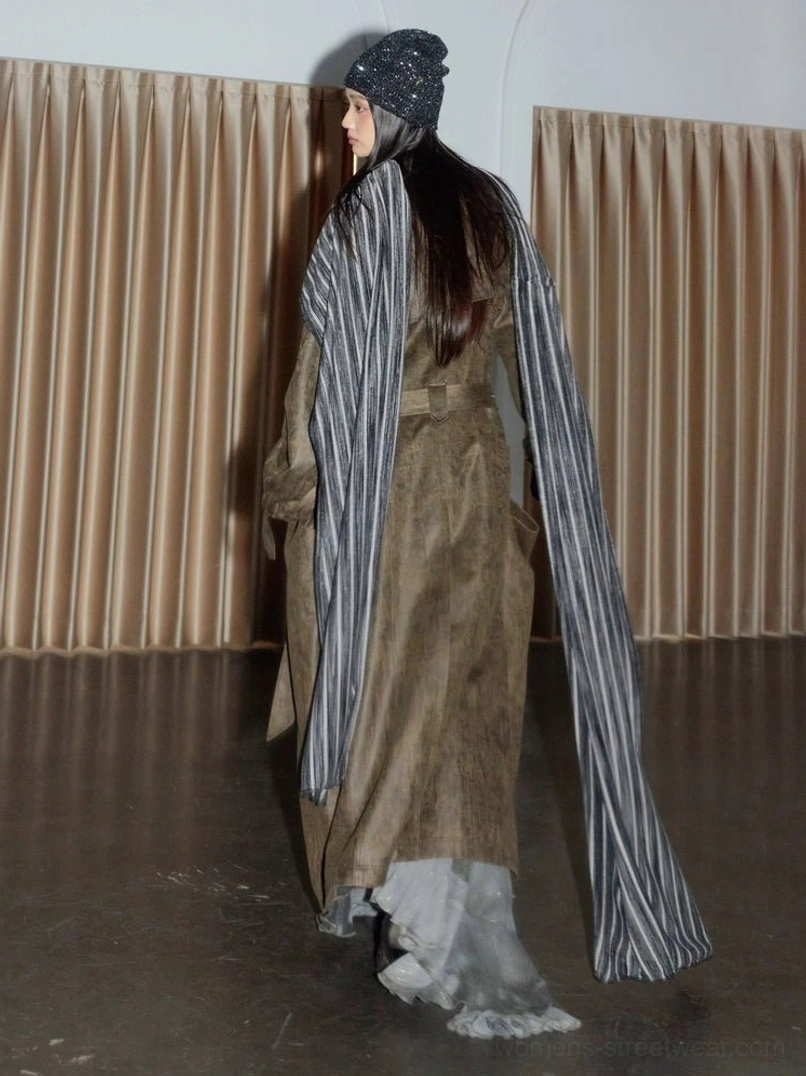 Back three-quarter view of a full-length distressed military green trench coat showing the back waist strap, long hem, and faded vintage utility finish