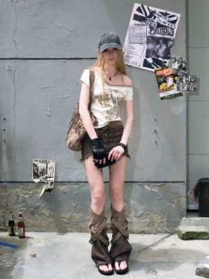 Women's distressed off-shoulder graphic top styled with brown shorts leg warmers baseball cap and vintage tote bag
