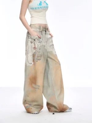 Front three-quarter view of distressed painted wide-leg blue jeans with faded brown wash patchwork panels and decorative metal chain details