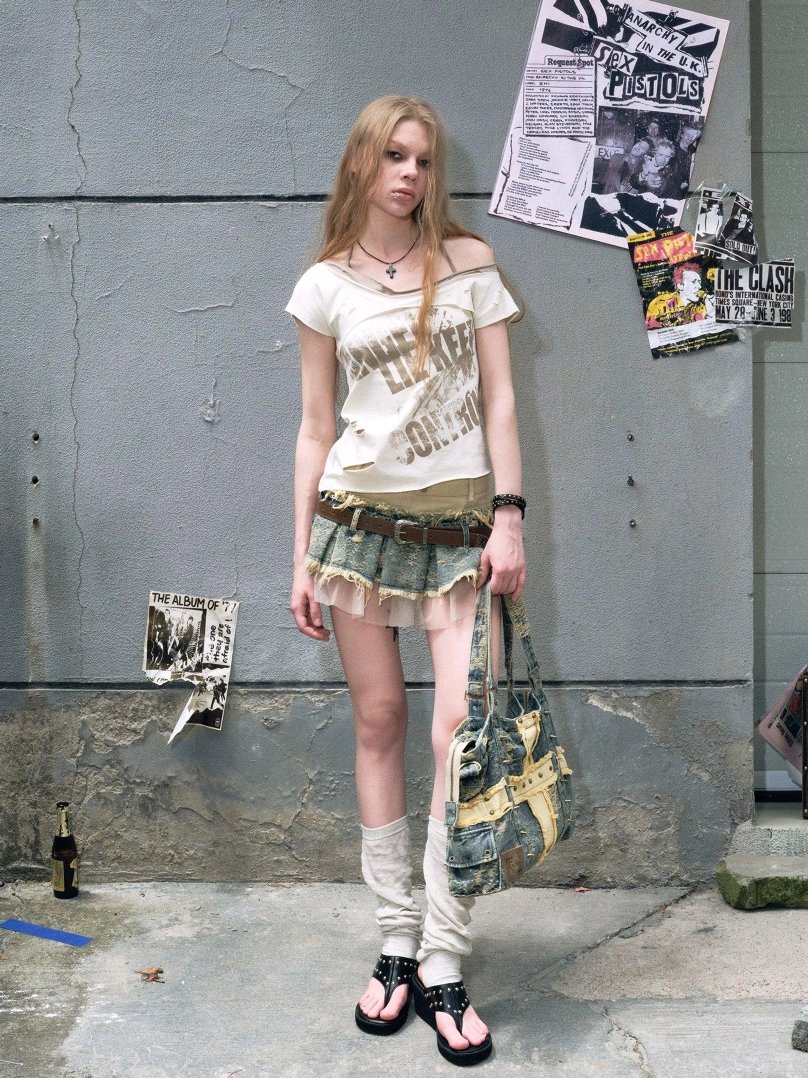 Full body streetwear outfit featuring a distressed patchwork denim mini skirt, sheer tulle layer, brown belt, denim tote bag, and sandals