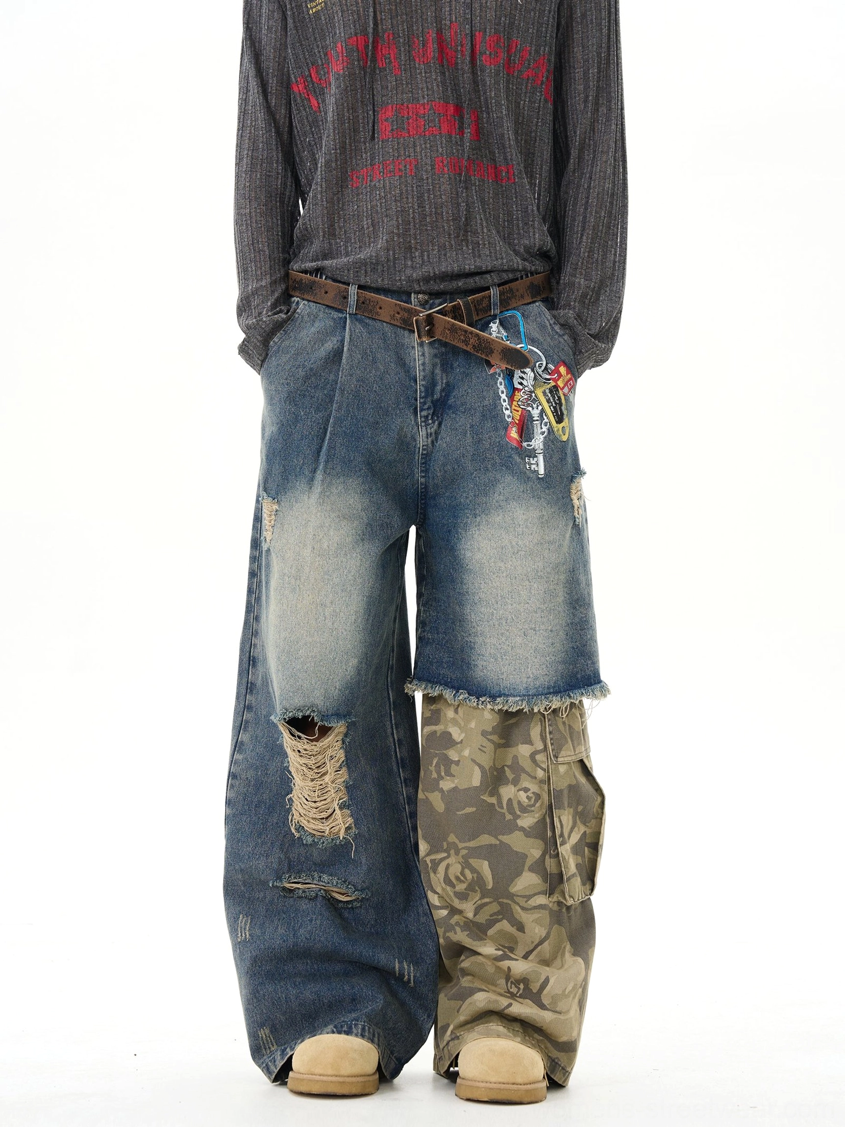 Front view of distressed patchwork wide-leg jeans on a male model, showing vintage washed blue denim, camo cargo panels, ripped frayed details, and decorative keychain-style embroidery
