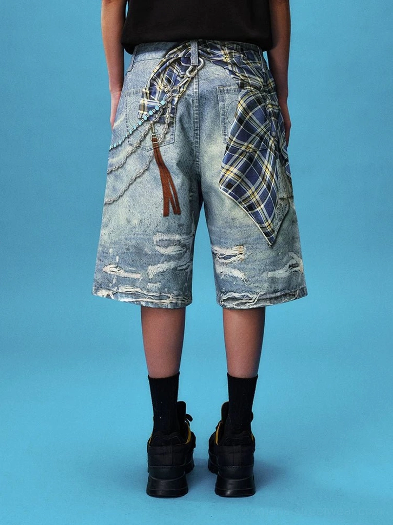 Full back view of distressed washed blue denim jorts with plaid handkerchief detail, layered chain accents, leather tassel, and relaxed knee-length fit