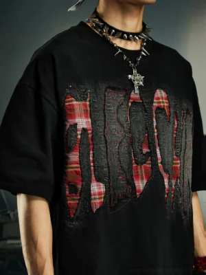 Close-up of black distressed plaid slash oversized graphic streetwear tee with layered red plaid chest lettering