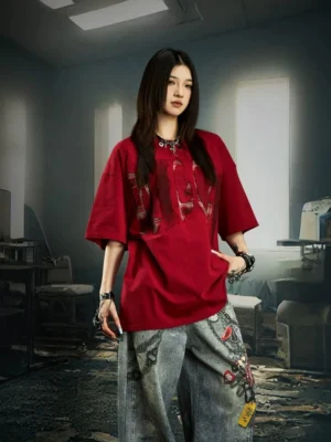 Red distressed plaid slash oversized graphic streetwear tee worn with embroidered wide-leg jeans in a vintage studio