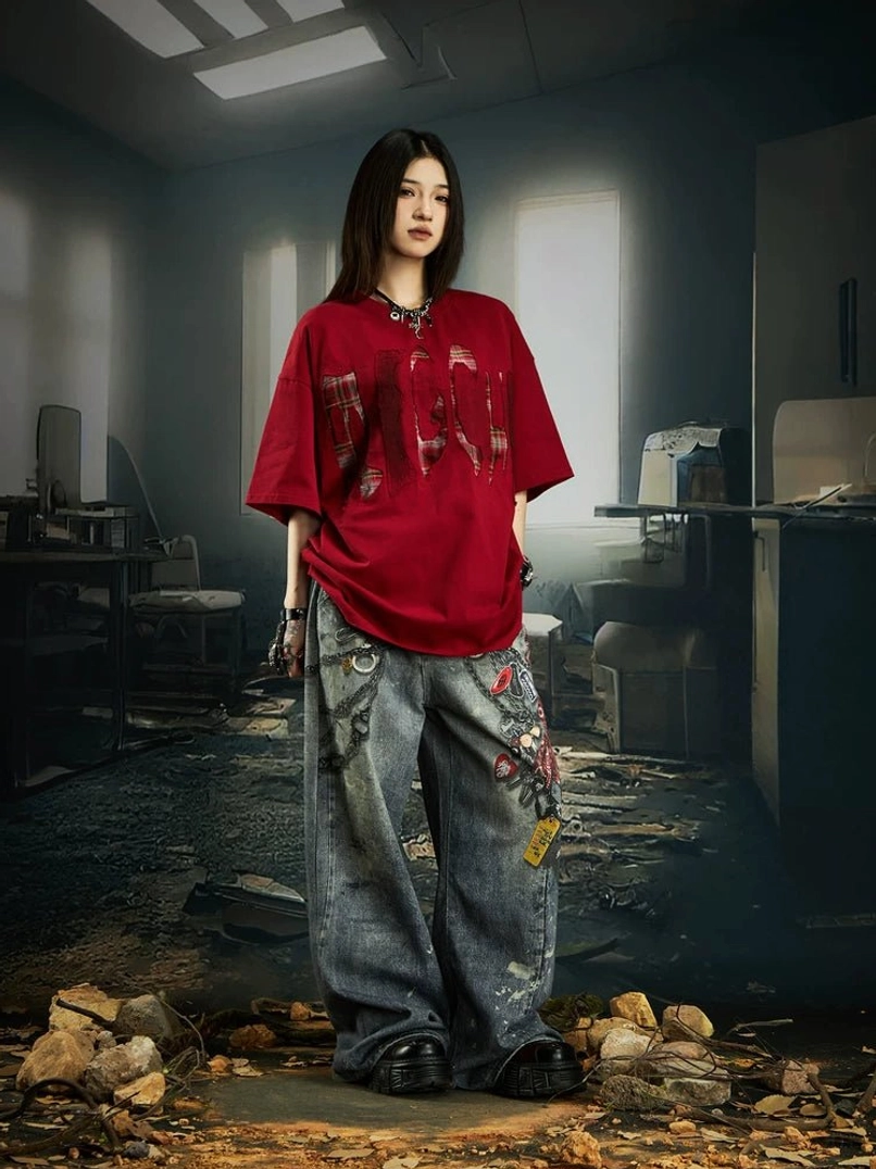 Red distressed plaid slash oversized graphic streetwear tee shown from a side-front angle with relaxed dropped shoulders