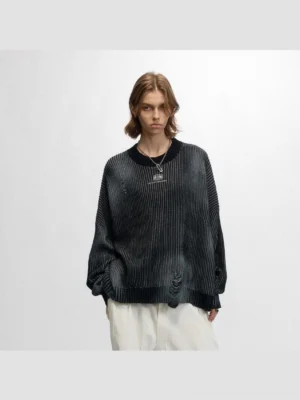 Front view of a model wearing a faded black distressed ribbed logo sweater with oversized drop shoulders and loose white trousers