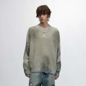 Front view of a male model wearing a sage gray distressed ribbed logo sweater with ripped denim jeans