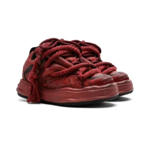 Burgundy distressed rope-lace chunky sneakers shown from a low front three-quarter angle with oversized braided tassel laces, matte layered upper, decorative stripe accents, and a thick weathered platform sole
