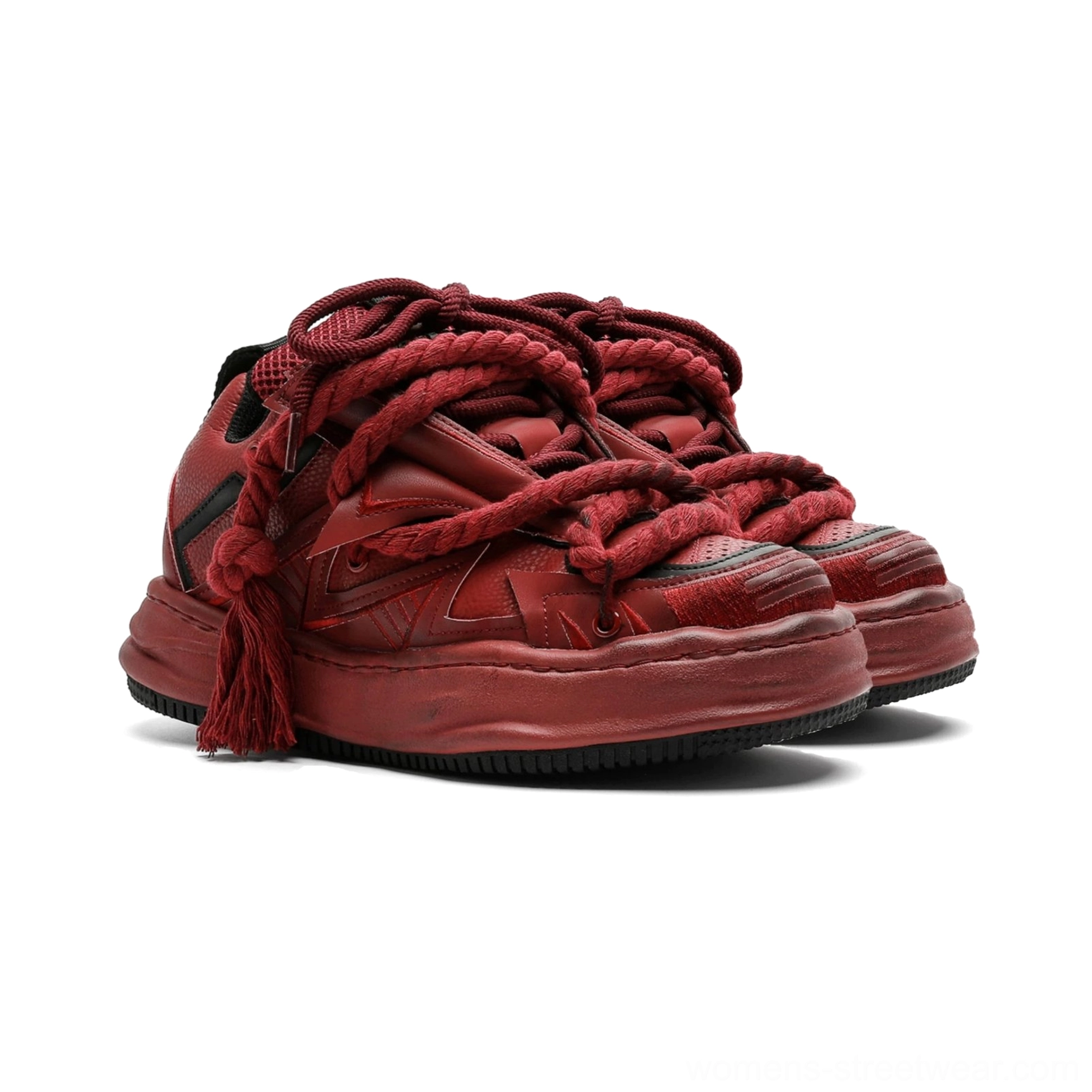 Burgundy distressed rope-lace chunky sneakers shown from a low front three-quarter angle with oversized braided tassel laces, matte layered upper, decorative stripe accents, and a thick weathered platform sole