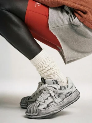 Distressed shell-toe leather skate sneaker worn with thick knitted socks and mixed-tone streetwear trousers in a low rear three-quarter studio view