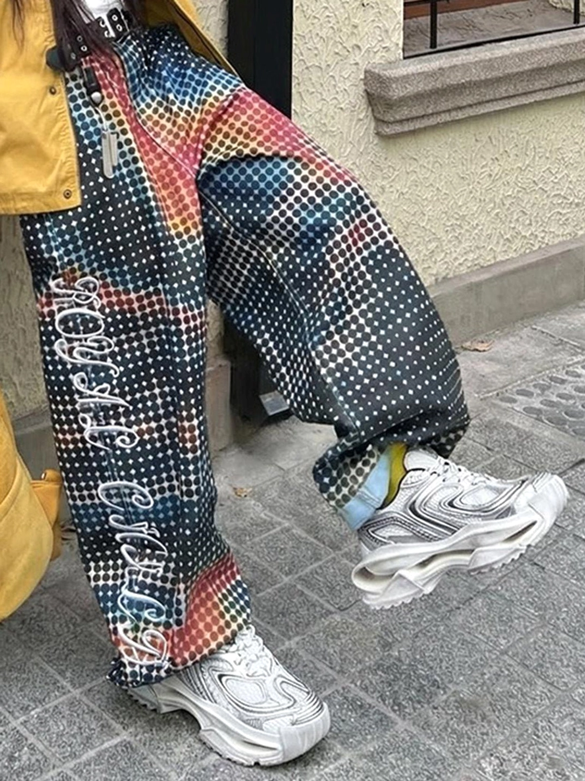 Low-angle side view of distressed silver sculpted sole sneakers worn with embroidered checkered pants on city pavement