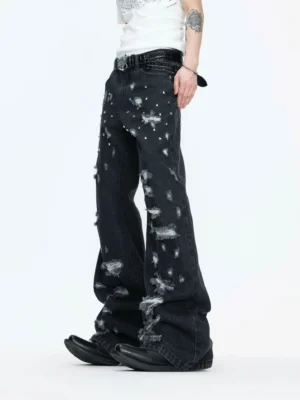 Low-angle view of washed black distressed studded wide-leg jeans with frayed ripped details, silver metallic studs, and an elongated streetwear silhouette