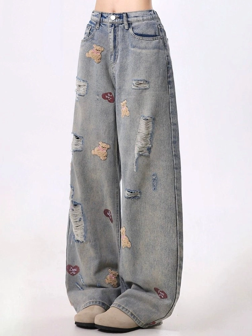Front low angle view of distressed teddy bear embroidered wide-leg jeans with vintage washed blue denim, red heart details, frayed rips, high waist, and belt loops