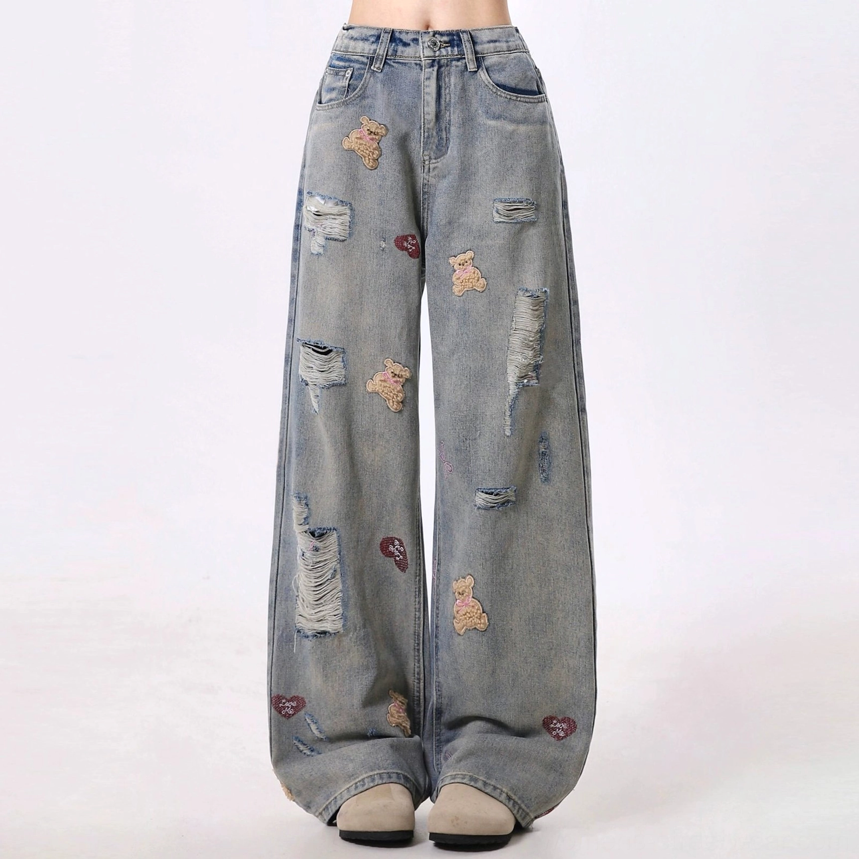Front view of distressed teddy bear embroidered wide-leg jeans with prominent ripped details, vintage denim wash, and high-waisted streetwear silhouette